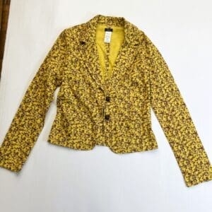 A yellow blazer with a purple floral pattern, three front buttons, and long sleeves is laid flat on a white surface.