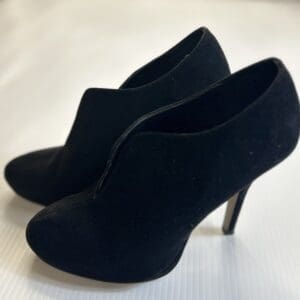 A pair of black high-heeled ankle boots made of suede material, placed on a white surface.