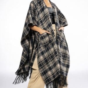 A person wearing a long, black and beige plaid fringe poncho over a Tapered Waist Button Down Shirt and beige wide-leg pants with black shoes, standing against a plain white background.