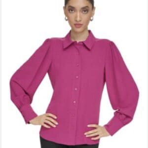 A woman wears the Tapered Waist Button Down Shirt in bright pink with long puffed sleeves and black pants, standing with hands on hips against a plain background.
