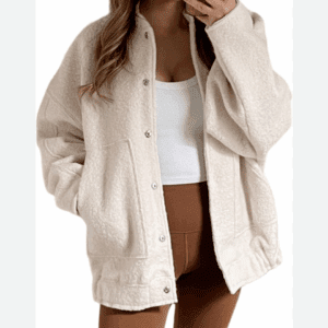 A person wearing Popeye's Button up Sweater in cream over a white tank top and brown leggings, holding a phone and posing with one hand in their pocket.