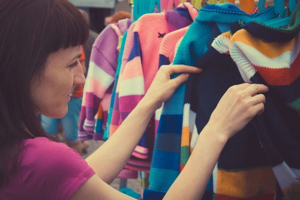 A woman examines colorful striped sweaters on a clothing rack.