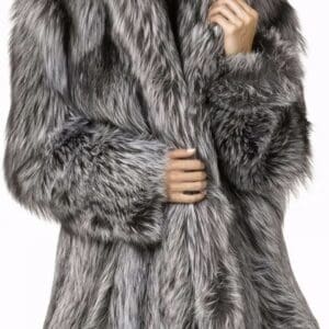 A woman wears a thick, luxurious faux fur coat in silver and gray tones, standing against a plain white background.