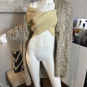 A white mannequin wears a beige knit wrap top and a textured brown cardigan, displayed in a modern room with a bar cart and decorative pillow in the background.
