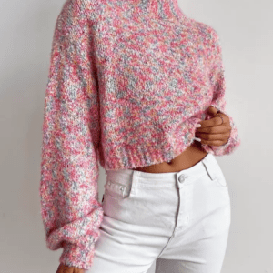 A person wearing a cropped, multicolored pink knit sweater with long sleeves and high-waisted white jeans stands against a plain white background.