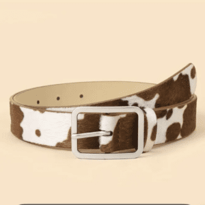 A brown and white cow print Product with a rectangular silver buckle is displayed against a plain beige background.