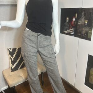 A mannequin dressed in a black tank top and gray jogger pants stands indoors near a cabinet with bottles and a bench with a chevron pillow.