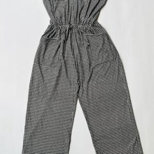 Product laid flat on a white background: a sleeveless black and white checkered jumpsuit with spaghetti straps and an elastic waist.