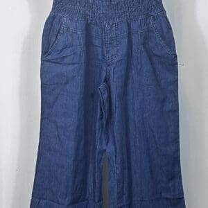 The Product is a blue denim strapless jumpsuit with a smocked bodice, chest buttons, wide legs, and side pockets, displayed on a black hanger.