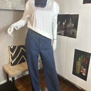 A mannequin dressed in a white long-sleeve shirt, blue jeans, and a navy cap with an orange "W," standing beside a bar cabinet and a patterned pillow on a bench.