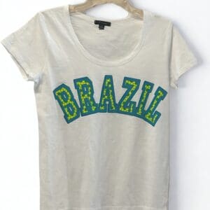A white short-sleeve T-shirt with the word "BRAZIL" in large blue and yellow letters printed on the front, hanging on a plastic hanger against a white background.
