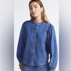 A woman wears the Denim Volume Sleeve Shirt SIZE S—a blue, long-sleeve denim button-up—paired with blue jeans, standing against a plain light background.