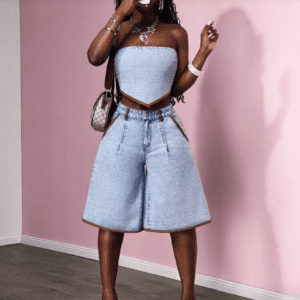 A woman poses against a pink wall, wearing Slaydiva Women Trim Flared Denim Shorts (Size 26), a denim bandeau top, heeled sandals, a choker necklace, and holding her phone in front of her face.