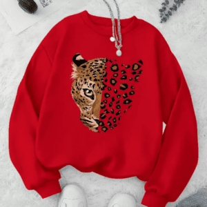The Women's Crew Neck Cheetah Lightweight Sweatshirt (Size M) is a red top with a half-detailed, half-spotted cheetah face graphic, shown paired with a necklace, white shoes, and headphones.