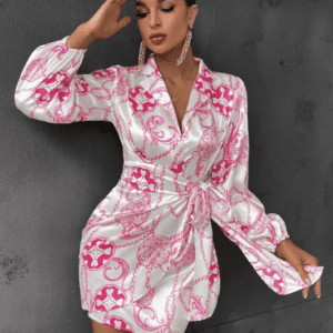 Woman wearing a long-sleeve, belted satin dress with pink and white chain patterns, posing against a dark textured wall.