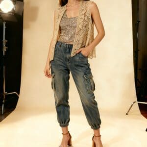 A person wears a Sleeveless Lace Open Front Short Cardigan (Chico's Size 3) over a patterned top, styled with cargo jogger jeans and heeled sandals, posing in a professionally lit photo studio.
