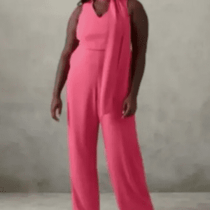Person wearing a sleeveless, wide-leg pink jumpsuit with a matching scarf, standing against a plain, light-colored background.