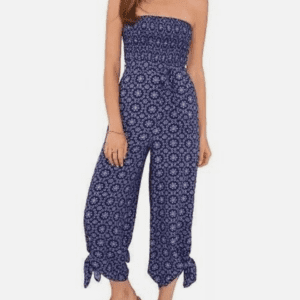 Woman wearing a strapless, navy blue jumpsuit with a white floral pattern, cropped wide legs tied at the ankles, and brown slide sandals.