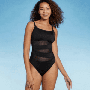 Woman wearing a black one-piece swimsuit with sheer panel details, standing and smiling against a blue background.