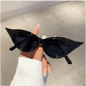 A hand with long, manicured nails holds a pair of black cat-eye sunglasses against a neutral tiled background.