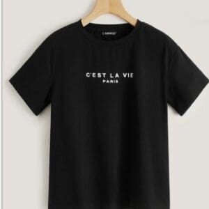 A black short-sleeve t-shirt on a wooden hanger with the text “C’EST LA VIE PARIS” printed in white on the front.