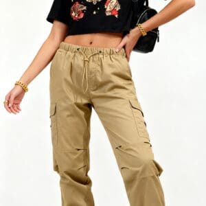 Woman in a black cap, graphic black crop top, khaki cargo pants, and black combat boots, posing with one hand on hip and a black bag over her shoulder.