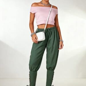 Woman standing wearing a pink off-shoulder crop top, green jogger pants with lace-up ankles, pink and white sneakers, and a white crossbody bag.