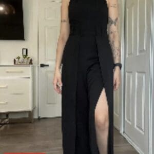 Person wearing a sleeveless black jumpsuit with a high leg slit, standing indoors on wooden flooring; "15% OFF" label shown in bottom left corner.