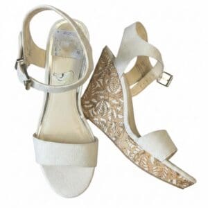 A pair of white wedge sandals with ankle straps and floral cutout details on the wedge heels, shown on a white background.