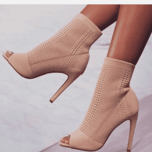 A person wears nude, open-toe, high-heeled ankle boots with a perforated knit design, shown against a neutral background.