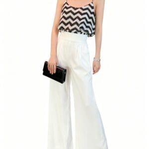 Woman wearing a black and white zigzag sleeveless top, high-waisted white wide-leg pants, black sandals, and holding a black clutch against a white background.