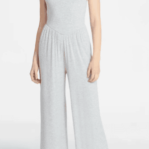 A woman wearing a light gray sleeveless jumpsuit with wide legs and spaghetti straps stands against a plain white background.