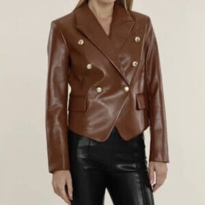 A woman wears a brown double-breasted faux leather blazer with gold buttons and black leather pants.