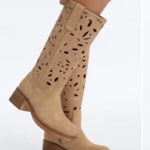 Tan knee-high boots with chunky heels and decorative cut-out floral patterns, worn by a person against a plain background.