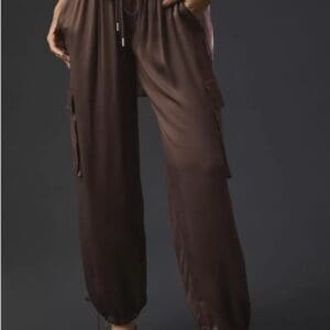 Person wearing loose brown cargo pants with drawstring waist and side pockets, hands in pockets, standing against a plain dark background.
