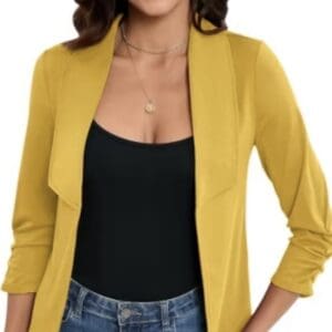 A woman wearing a yellow blazer over a black top and blue jeans, with a necklace and hoop earrings, is shown from the shoulders to hips.