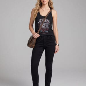 Woman standing against a plain background, wearing a black NY cap, a black graphic tank top, black pants, white sneakers, and a brown crossbody bag.