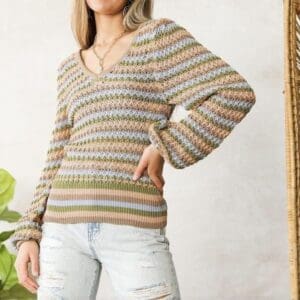 A woman wearing a V-neck, multi-colored striped knit sweater with long, billowed sleeves.