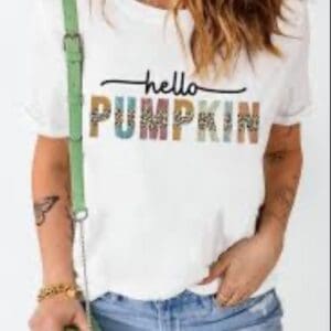 A woman wearing a white t-shirt that says “hello PUMPKIN” in leopard print and multicolored letters.