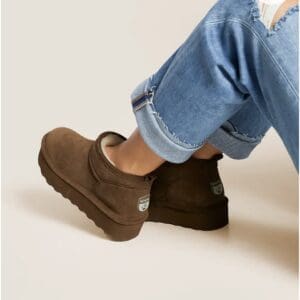 A person wearing brown Bearpaw platform ankle boots and cuffed, distressed blue jeans.
