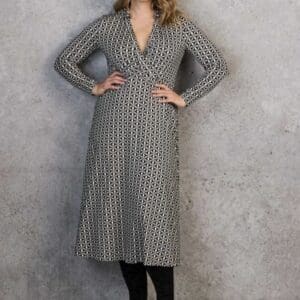 A woman wearing a long-sleeved midi dress with a geometric black and white pattern and black boots.
