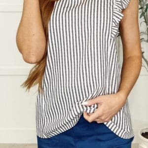 A person wearing a sleeveless black and white striped top with ruffled shoulders and blue pants.