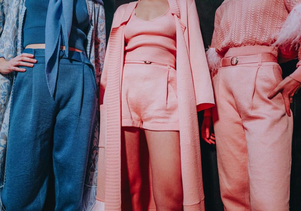 Three people stand side by side, each wearing stylish, textured outfits in shades of blue and pink, with the photo showing them from shoulders to knees.