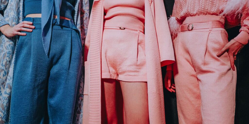 Three people stand side by side, each wearing stylish, textured outfits in shades of blue and pink, with the photo showing them from shoulders to knees.