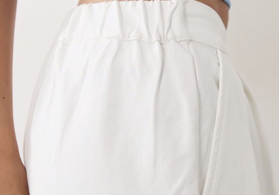 A person wearing a light blue crop top and high-waisted white pants with an elastic waistband, shown from the torso down.