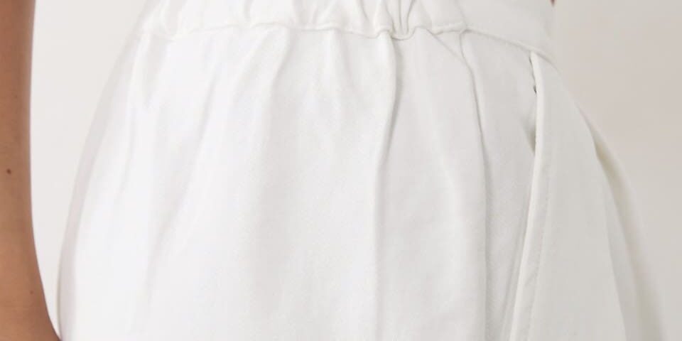 A person wearing a light blue crop top and high-waisted white pants with an elastic waistband, shown from the torso down.