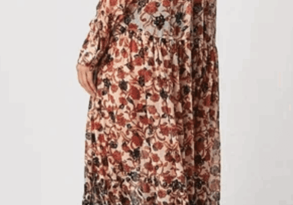 Model wears the Long, Long Sleeve Sheer Flowered Dress, an ankle-length floral piece with ruffled hem, paired with black boots; shown from the back against a plain background.