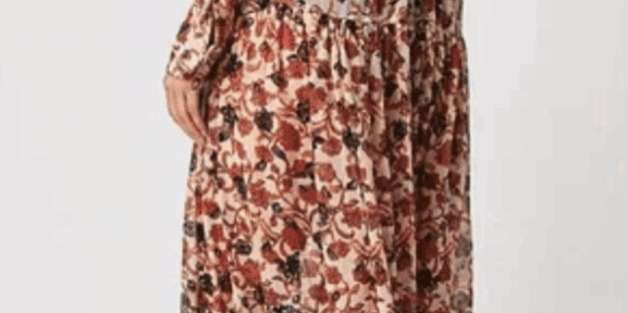 Model wears the Long, Long Sleeve Sheer Flowered Dress, an ankle-length floral piece with ruffled hem, paired with black boots; shown from the back against a plain background.
