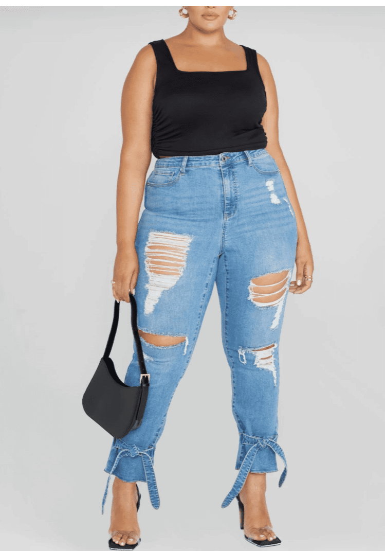 A person wearing a black sleeveless top, Denim Ripped Belted Ankle Jeans with tied hems, holding a black handbag, and wearing clear-strap heels.