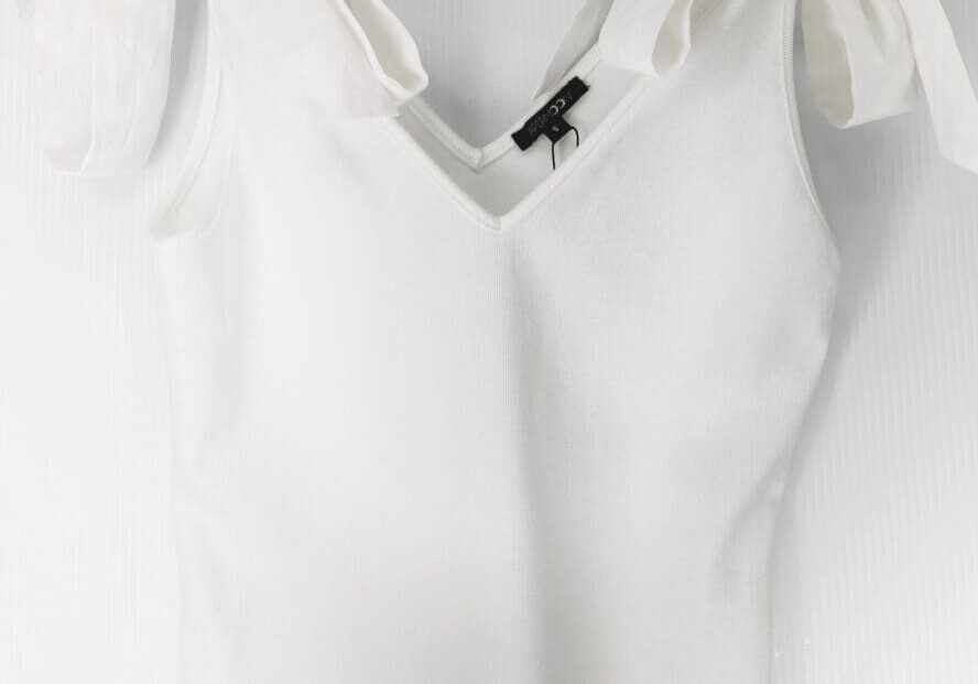 The White Tie Shoulder Top is a sleeveless V-neck with wide shoulder straps tied in bows, shown on a clear plastic hanger against a light background.